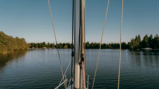 Sailboat sails on serene water toward trees.