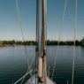 Sailboat sails on serene water toward trees.